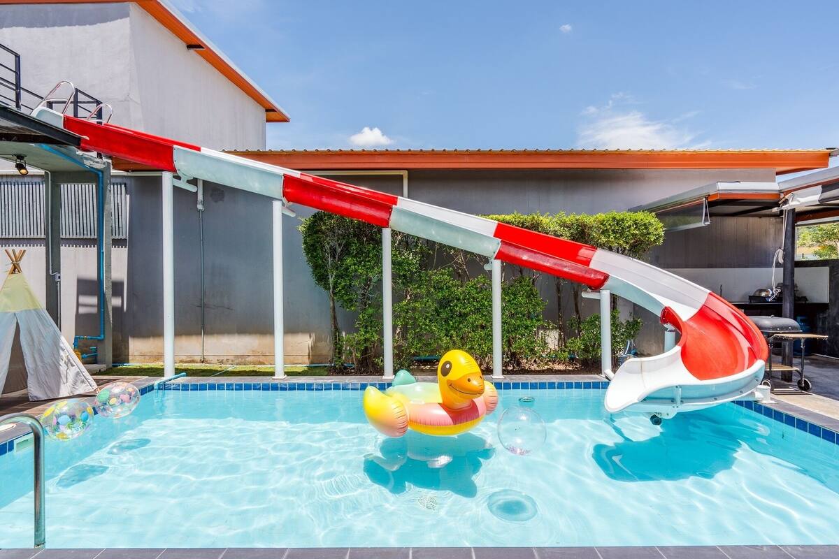 A swimming pool with a water slide, a duck float, and a tent.