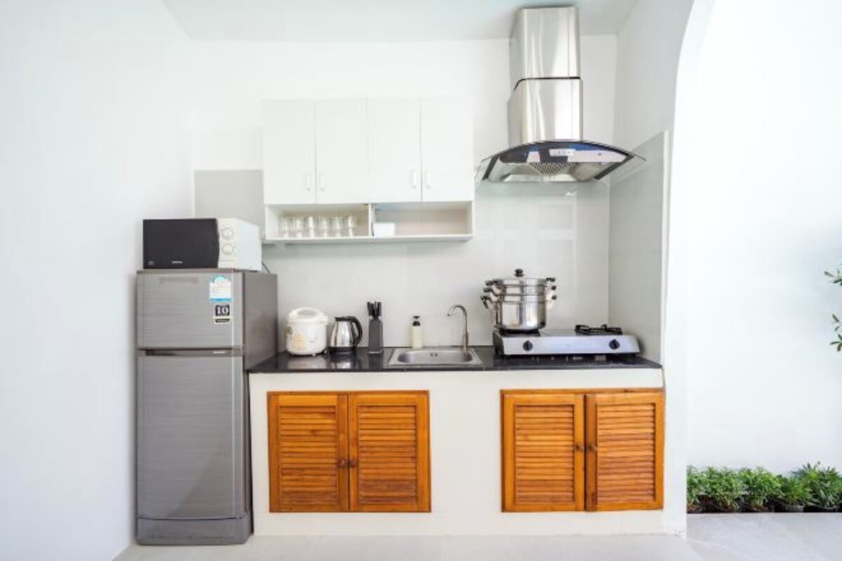A compact kitchen with a stainless steel refrigerator, wooden cabinets, a gas stove, and a microwave.