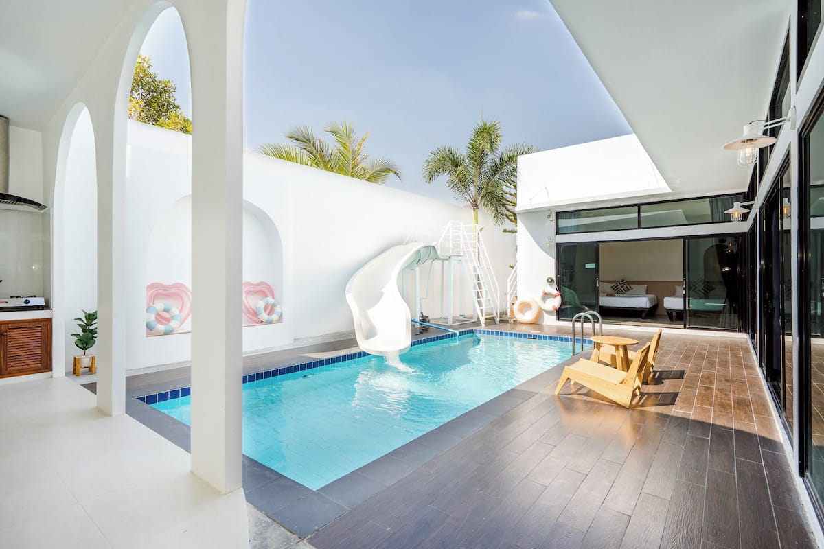 A modern indoor swimming pool with a clear view of the sky, a sun lounger, and a ladder leading to a slide.