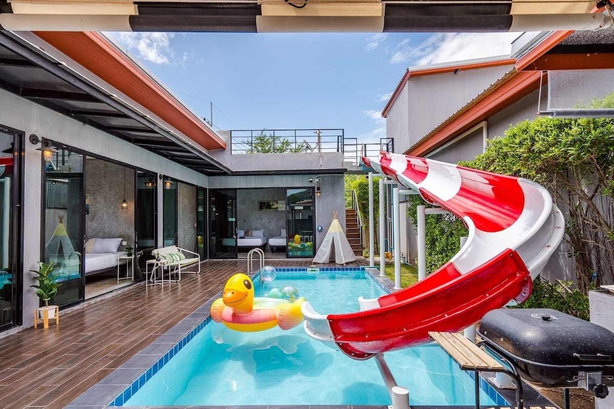 A modern outdoor pool area with a slide, lounge chairs, and a tent-like structure.