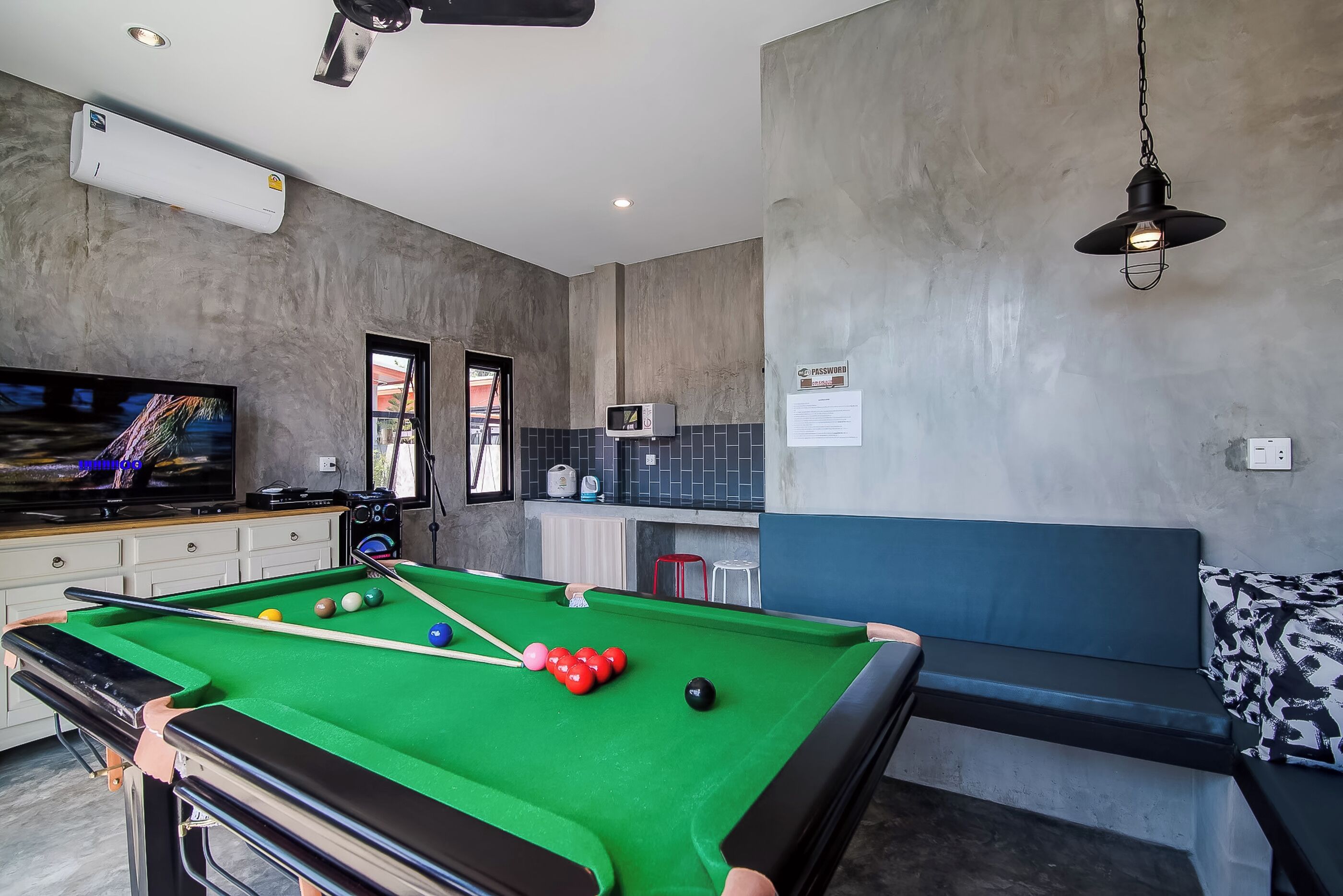 A pool table with balls, a television, and a seating area with a blue bench.