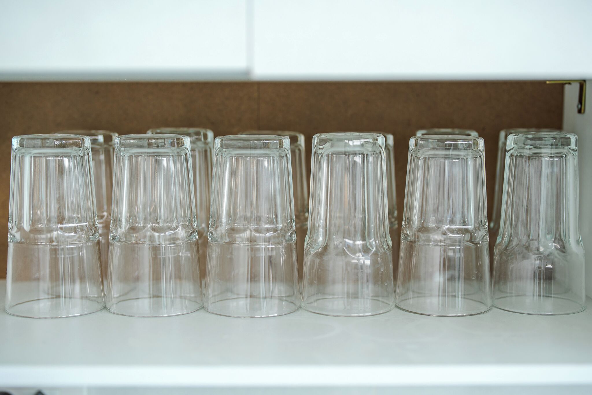 A row of empty glass tumblers on a shelf.