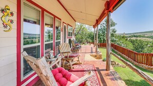 A covered porch with a red railing, a wooden chair, a red cushioned chair, and a dining table with chairs. - Medicine Park Cottage: Walk to Lake Lawtonka! (Medicine Park)