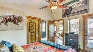 A bedroom with a large bed, a ceiling fan, a door leading to another room, and a painting of a bull on the wall. - Medicine Park Cottage: Walk to Lake Lawtonka! (Medicine Park)