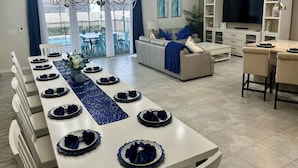 Una sala moderna con comedor listo para una comida, un sofá, un televisor y vistas al exterior.