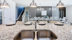 Una cocina moderna con encimeras de granito, lavamanos de acero inoxidable e iluminación colgante.