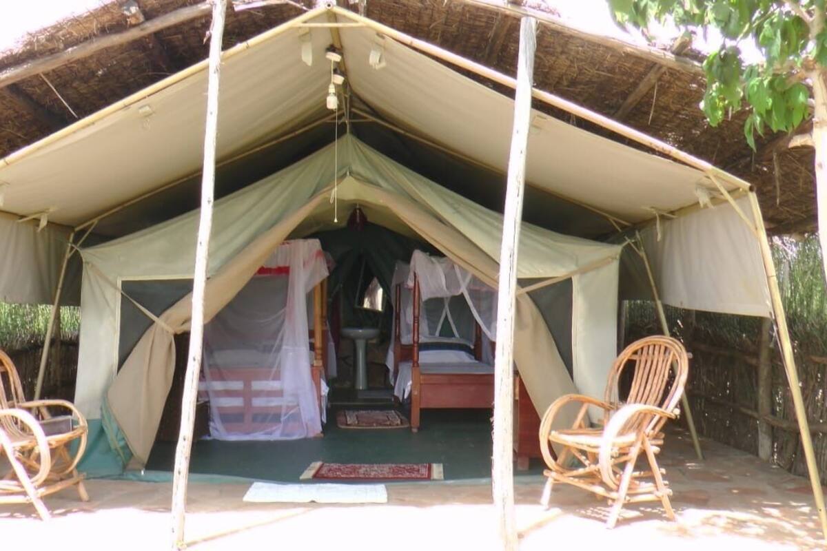 Una carpa con techo de paja, dos sillas de madera, una cama y una pequeña mesa con un libro.
