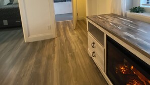 A room with a wooden floor, a built-in entertainment unit, a window with blinds, and a door leading to another room. - Fabulous entire 2-bedroom house with onsite washer/dryer in Richmond near Bart. (Richmond)