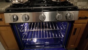 An open oven with a blue interior, a stove with pots and pans, and a digital clock displaying 11:02. - Fabulous entire 2-bedroom house with onsite washer/dryer in Richmond near Bart. (Richmond)