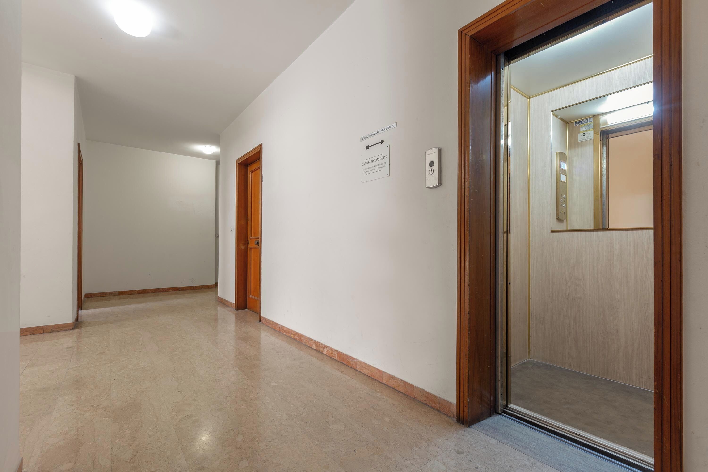 A hallway with a wooden door, a wall-mounted light switch, and an elevator door.
