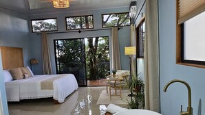 Une chambre spacieuse avec un grand lit, un coin salon avec une baignoire blanche et une vue sur l’extérieur.