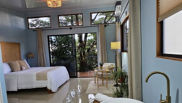 A spacious bedroom with a large bed, a sitting area with a white bathtub, and a view of the outdoors.