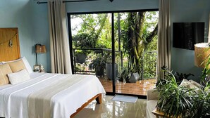 A bedroom with a bed, a chair, a TV, and a view of greenery through a glass door.