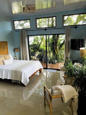 A bedroom with a bed, a sofa, a TV, and a large window with a view of trees.