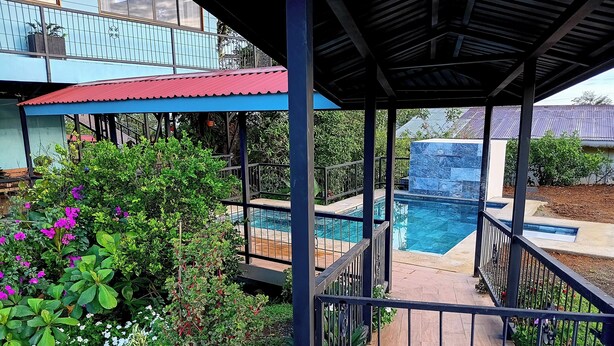 Un espace extérieur abrité, doté d’une piscine, entouré d’une végétation luxuriante et d’une rambarde en métal.