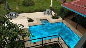 A swimming pool with a stone border, surrounded by a deck with outdoor furniture and a covered seating area.