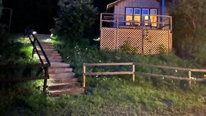 A wooden cabin with a balcony, surrounded by greenery and a staircase leading up to it. - Expedition Everest Cabin At Basecamp (Saint Johnsbury)