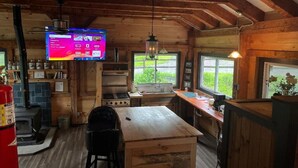 A rustic cabin interior with a wooden dining table, a kitchen with a stove, and a television displaying Netflix. - Expedition Everest Cabin At Basecamp (Saint Johnsbury)