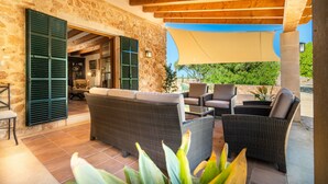 Eine Terrasse im Freien mit Korbmöbeln, Steinmauern und einer Holzbalkendecke.