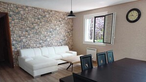 A modern living room with a stone wall, white sofa, dining table, and chairs. - Comfortable villa with pool in the countryside (Foissiat)