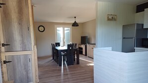 A spacious kitchen with a refrigerator, a dining area with chairs, a wooden door, and a wall clock. - Comfortable villa with pool in the countryside (Foissiat)