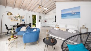 A modern, well-lit room with a bed, blue chairs, a dining area, and a kitchen.