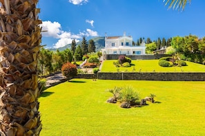 Ein großes, weißes, zweistöckiges Haus mit einem gepflegten Rasen und Garten, umgeben von Bäumen und Hügeln.