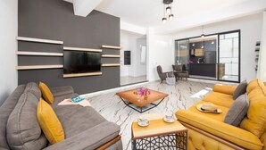 Ein modernes Wohnzimmer mit Flachbildfernseher, einer Couch, einem Couchtisch und einem Esstisch mit Stühlen.