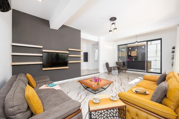 Una sala de estar moderna con un televisor de pantalla plana, un sofá, una mesa de centro y una mesa de comedor con sillas.