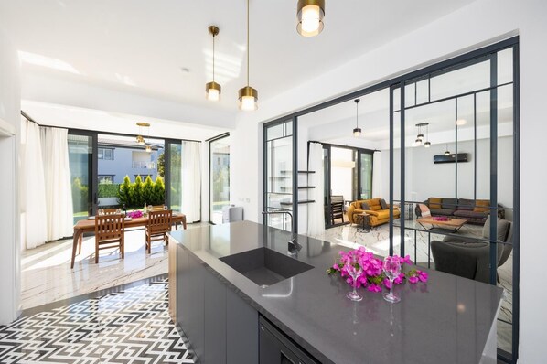 Una cocina moderna con una isla grande, un comedor con mesa y sillas, y una sala de estar con sofá y mesa de centro.