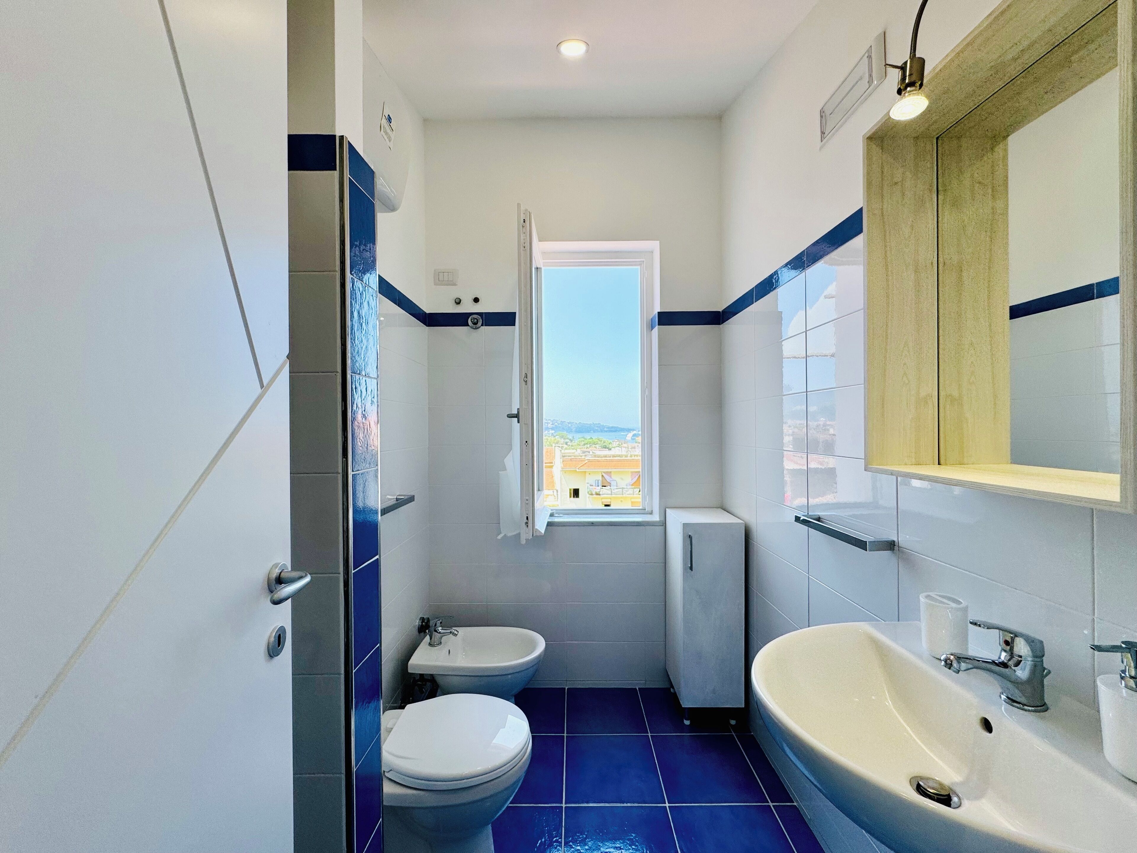 A bathroom with a toilet, bidet, and sink, a window with a view, and a mirror above the sink.