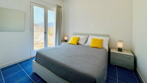 A bedroom with a bed, two bedside tables, a nightstand, a window with curtains, and an air conditioning unit. - YourHome - La Famiglia Apartment (Meta)