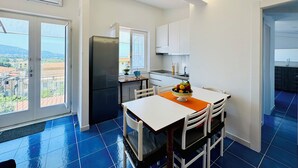 A modern kitchen with a black refrigerator, white cabinets, and a dining area with a table and chairs. - YourHome - La Famiglia Apartment (Meta)