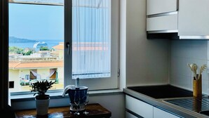 A kitchen with a view of the sea, a potted plant, a bottle of champagne, and two wine glasses on a table. - YourHome - La Famiglia Apartment (Meta)