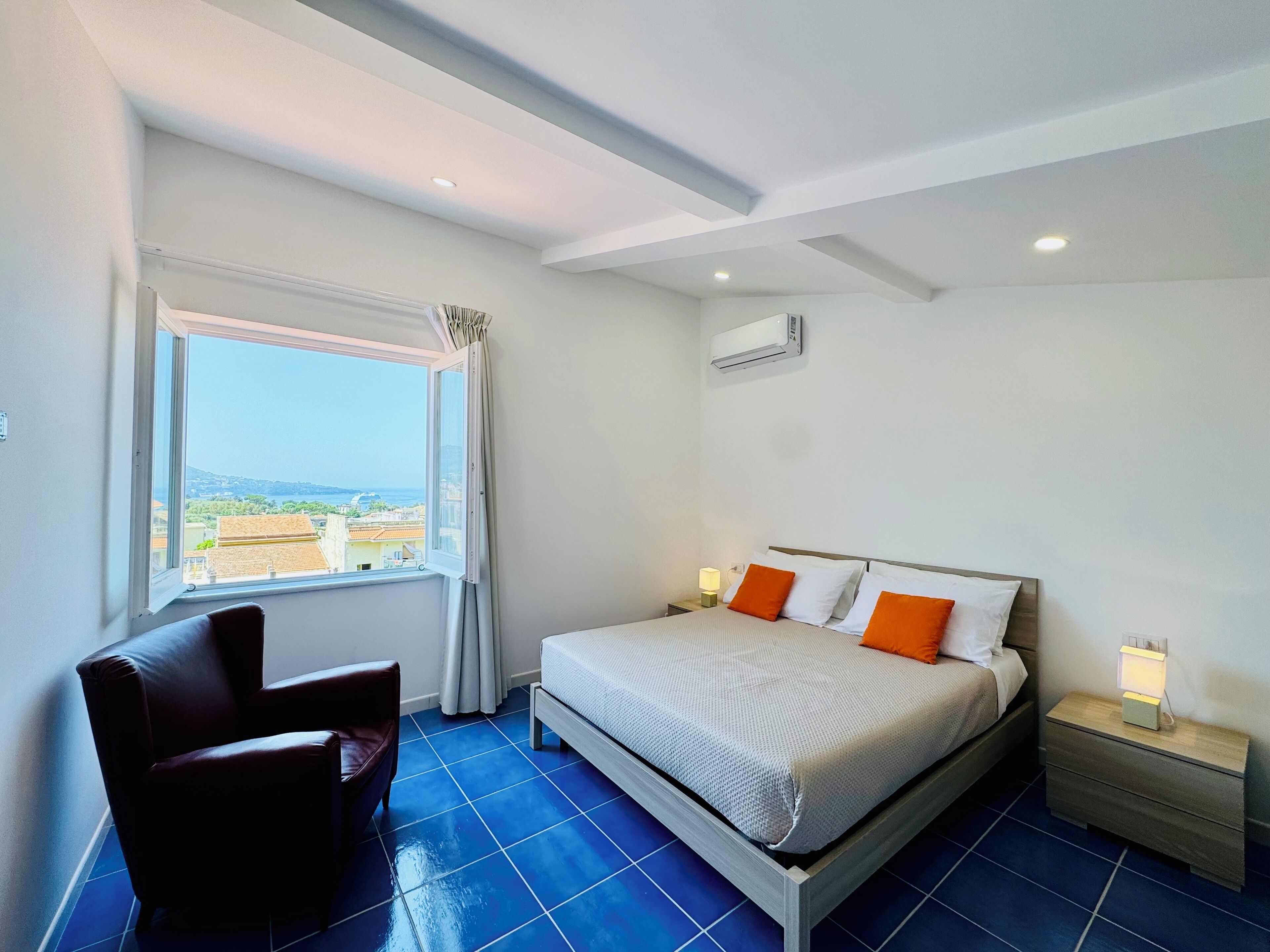 Quarto com cama, cadeira, mesa de cabeceira e janela com vista.
