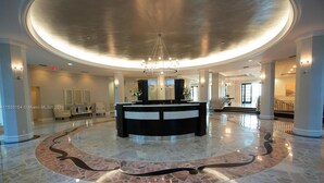 A spacious lobby with a central reception desk, a chandelier, and a circular marble floor design. - 1BD/1.5BTH BeachFront Resort Style. Gym, WiFi, Free Parking, Jacuzzi, GameRoom. (Hollywood)