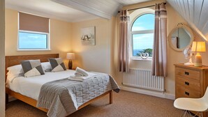 A bedroom with a bed, bedside table, lamp, and a view of the sea.
