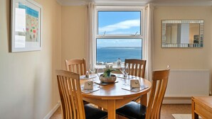 A dining area with a round wooden table, four chairs, and a view of the sea through a large window.