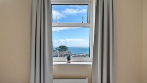 Una habitación con ventana que da a un cuerpo de agua y edificios, un radiador debajo de la ventana y una pequeña planta en maceta sobre el alféizar.