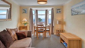 Habitación de hotel con zona de comedor, sofá, lámpara y vista al mar.