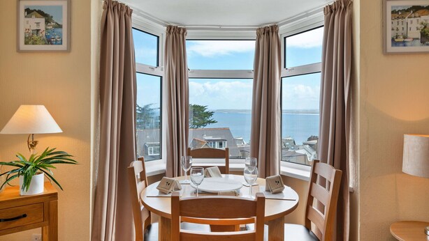 Un comedor con una mesa dispuesta para cuatro personas, una planta en maceta y vista al mar a través de amplios ventanales.