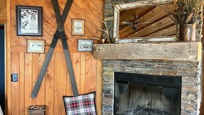 A cozy living room with a stone fireplace, wooden walls, and a ski-themed decor.