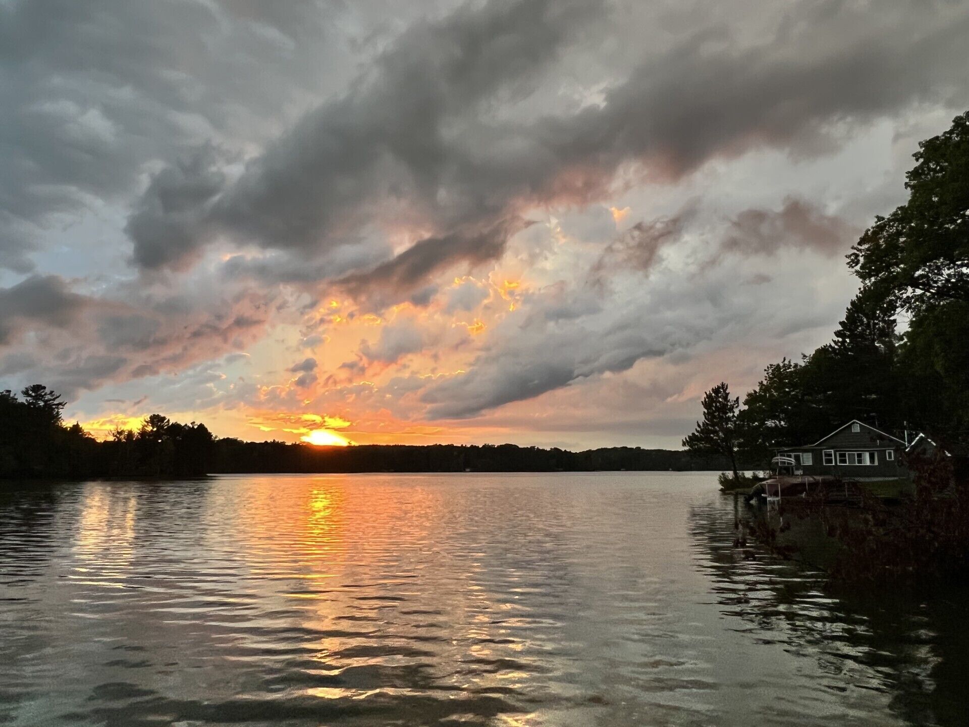 Un coucher de soleil sur un lac, avec une maison sur la droite.