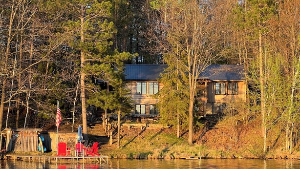 A lakeside cabin with a dock, surrounded by trees and a clear view of the water.