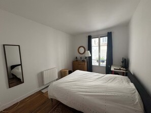 A bedroom with a bed, a dresser, a mirror, a window with curtains, and a radiator.
