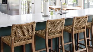 Una cocina moderna con una isla grande, taburetes de bar, un refrigerador de acero inoxidable y vistas al exterior a través de amplios ventanales.