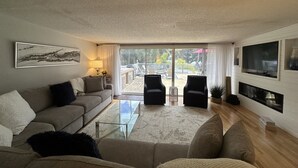A living room with a sofa, armchairs, a coffee table, and a TV. There is a sliding glass door leading to an outdoor area with a patio and a view of greenery. - Siesta Key Access- Large Deck w/ Bay View: 2-Bdrm Condo-sleeps 6 Heated Pool! (Sarasota)