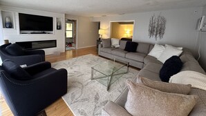 A modern living room with a flat-screen TV, a glass coffee table, and a grey sofa with multiple cushions. - Siesta Key Access- Large Deck w/ Bay View: 2-Bdrm Condo-sleeps 6 Heated Pool! (Sarasota)