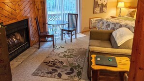 A cozy hotel room with a fireplace, a dining table with chairs, a sofa, a bed, and a painting on the wall. - The Springbrook  Inn - Forrest View Room (Hot Tub) (Denton Township)
