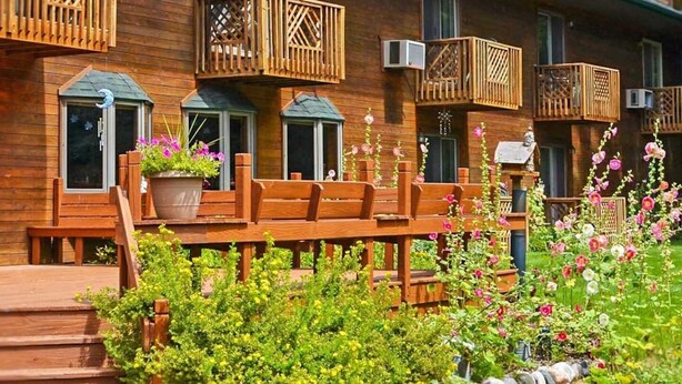 A wooden cabin with multiple balconies, a wooden deck, and a garden with flowers. - The Springbrook  Inn - Forrest View Room (Hot Tub) (Denton Township)